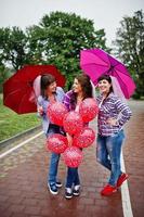 groupe de trois filles s'amusant à la fête de poule, avec parapluie sous la pluie et ballons. photo