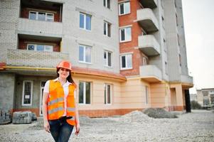 ingénieur constructeur femme en gilet uniforme et casque de protection orange contre le nouveau bâtiment. thème de bloc de vie de propriété. photo