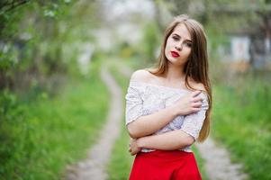 portrait de belle fille aux lèvres rouges au jardin de fleurs de printemps, porter une robe rouge et un chemisier blanc. photo