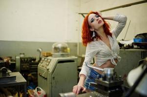 fille aux cheveux rouges portant un short en jean court et un chemisier blanc posé sur une machine industrielle à l'usine. photo