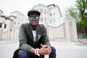 portrait en gros plan d'un homme afro-américain élégant portant des lunettes de soleil et une casquette en plein air. homme noir de mode de rue. photo