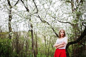 portrait de belle fille aux lèvres rouges au jardin de fleurs de printemps, porter une robe rouge et un chemisier blanc. photo