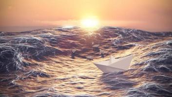 coucher de soleil avec bateau en papier combattant la vague dans l'océan, le leadership et le concept d'entreprise photo