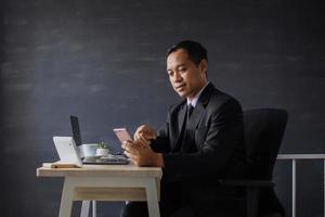 homme d'affaires asiatique souriant regardant et pointant vers le téléphone intelligent sur le bureau photo