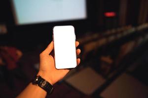 la main d'un homme adulte tient une maquette de téléphone intelligent à écran blanc vierge dans le théâtre. photo