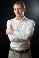 portrait en gros plan d'un jeune homme en chemise blanche et cravate noire, souriant en regardant la caméra, sur fond de studio uni photo