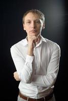 portrait en gros plan d'un jeune homme en chemise blanche et cravate noire, souriant en regardant la caméra, sur fond de studio uni photo