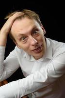 portrait en gros plan d'un jeune homme en chemise blanche et cravate noire, souriant en regardant la caméra, sur fond de studio uni photo