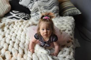 une petite fille avec une épingle à cheveux sur la tête est allongée sur le ventre sur le lit et regarde dans le cadre. photo