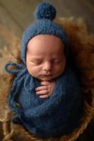 garçon nouveau-né dans un bonnet tricoté bleu et enroulement dort dans un panier sur un fond en bois. photo