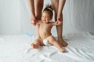 petite fille qui pleure sur un fond blanc. les mains du père tiennent l'enfant. photo