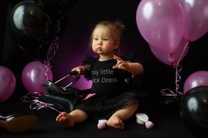 le jour de la fête d'anniversaire de la première année de la petite fille. ballons et vacances à l'intérieur. l'anniversaire de l'enfant. petite jolie fille dans sa première robe noire photo