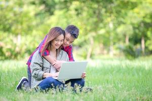 joyeuse mère et fils assis sur l'herbe étudiant avec un ordinateur portable dans le parc, concept d'apprentissage en plein air
