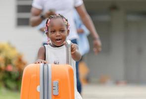 concepts de voyage, bagages orange avec une fille afro-américaine gaie et floue et une famille parentale quittant la maison pour les vacances photo