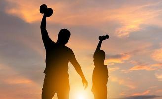 silhouette du père et du fils avec un tracé de détourage jouant à l'exercice avec haltère au coucher du soleil, concepts de famille de bonheur photo