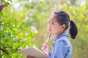 petite fille mignonne vérifiant les légumes et écrivant un document d'enregistrement dans une ferme, apprenant en dehors des concepts de la salle de classe. photo