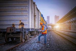 ingénieur chemin de fer en cours de vérification du processus de construction essai de train et vérification des travaux ferroviaires sur la gare avec communication radio .ingénieur portant un uniforme de sécurité et un casque de sécurité au travail. photo