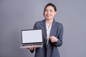 jeune femme d'affaires asiatique portant un costume et utilisant un ordinateur portable sur fond gris photo