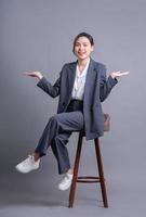 jeune femme d'affaires asiatique assise sur une chaise et posant sur fond gris photo