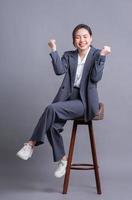 jeune femme d'affaires asiatique assise sur une chaise et posant sur fond gris photo