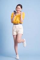 image pleine longueur d'une jeune femme asiatique utilisant un smartphone sur fond bleu photo