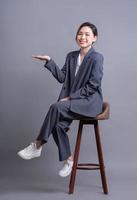 jeune femme d'affaires asiatique assise sur une chaise et posant sur fond gris photo