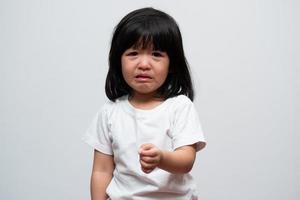 portrait d'une petite fille asiatique en colère, triste et en pleurs sur fond blanc isolé, l'émotion d'un enfant lorsqu'il est en colère et fou, expression d'émotion grincheuse. concept de contrôle émotionnel des enfants photo