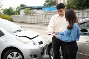 une conductrice asiatique parle à un agent d'assurance pour examiner la voiture endommagée et la vérification du client sur le formulaire de réclamation après un accident. concept d'assurance et d'accidents de la circulation automobile. photo