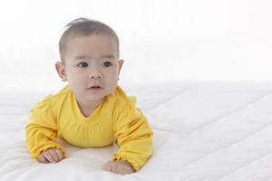 un bébé asiatique couché sur un lit blanc et propre.