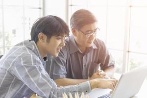 un homme asiatique âgé apprend à commercer en ligne via internet avec un jeune homme qui lui enseigne. photo