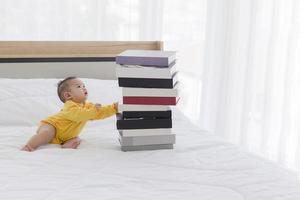 un bébé avec une pile de livres sur le lit.