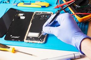 artisan en gants de caoutchouc répare ou entretient un téléphone portable sur un tapis en caoutchouc spécial pour réparation. vue de l'intérieur photo