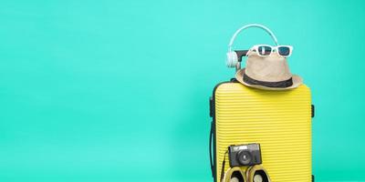 valise jaune avec lunettes de soleil, chapeau et appareil photo sur fond bleu pastel. notion de voyage. style minimaliste