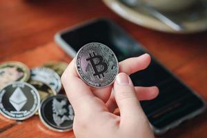 main de la femme tenant le bitcoin et le smartphone montrant le graphique boursier dans le café. concept d'argent virtuel de monnaie crypto. photo