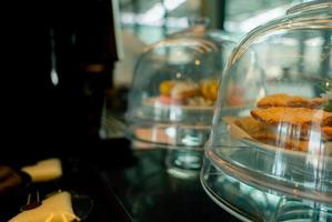 pâtisserie dans un présentoir en verre à gâteau avec dôme de couverture dans un café ou une boulangerie. pâtisserie dans le stand de gâteau sur le comptoir pour le service de buffet au restaurant. pâtisserie et café café pour les clients du service. photo