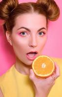 portrait d'élégante jolie jeune femme blonde avec des oranges sur fond rose photo