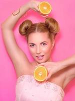 portrait d'élégante jolie jeune femme blonde avec des oranges sur fond rose photo