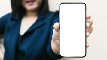 la main gauche d'une femme blanche montrant un téléphone portable ou un téléphone portable noir et un écran blanc pour le contenu de la maquette sur un fond blanc isolé ou découpé. photo