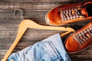 concept de mode homme. chaussures marron en cuir décontracté pour hommes, jeans et cintre sur fond sombre photo