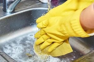 mains dans des gants jaunes nettoyant un évier dans la cuisine photo