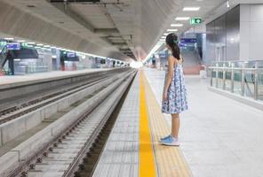 fille sur une gare, attendant le train, enfant attendant sur la plate-forme du tube, voyageant en chemin de fer. photo