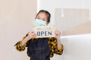 Petite fille asiatique portant un tablier happy face smiling with holding open sign wood board looking at the camera photo