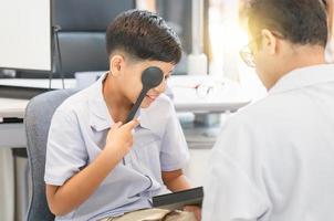 un garçon indien souriant faisant un examen de contrôle des yeux avec un optométriste dans un magasin d'optique photo