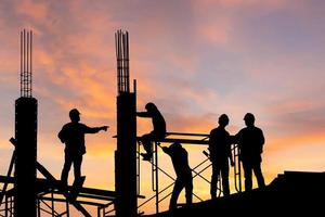 silhouette d'ingénieur et d'ouvrier sur chantier, chantier de construction au coucher du soleil en soirée.