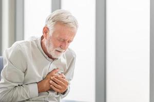 un homme âgé appuie la main sur la poitrine a une crise cardiaque souffre d'une douleur insupportable, un homme mûr avec une douleur au coeur dans le salon photo