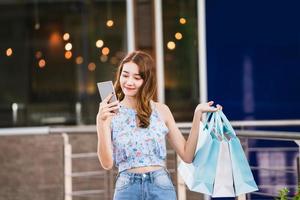 jeune femme shopper asiatique utilise un smartphone avec des sacs à provisions photo