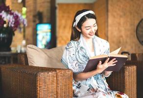 femme asiatique lisant un livre sur un canapé en osier. photo