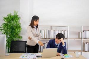 une femme chef asiatique se tenait dans une expression sérieuse, s'arrêtant avec un nouvel employé masculin assis sur une chaise. photo