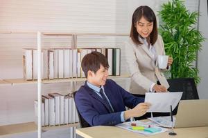 une collègue asiatique se tenait à parler à un homme d'affaires sur le bureau dans sa main tenant une tasse de café. photo