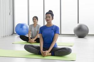 deux femmes asiatiques d'âge moyen faisant du yoga assises sur un tapis en caoutchouc dans une salle de sport. photo